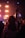 A scene of a concert or live event with a person in the foreground, silhouetted against bright stage lights. The hand is raised, conveying enthusiasm and engagement with the performance. Other audience members are visible facing the stage where performers are slightly blurred.