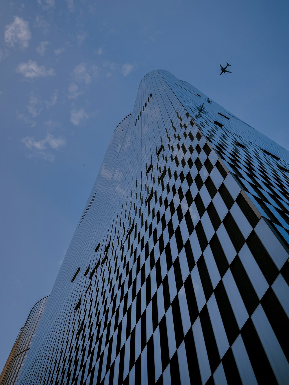 市松模様のデザインの高層ビルの上空を飛ぶ飛行機