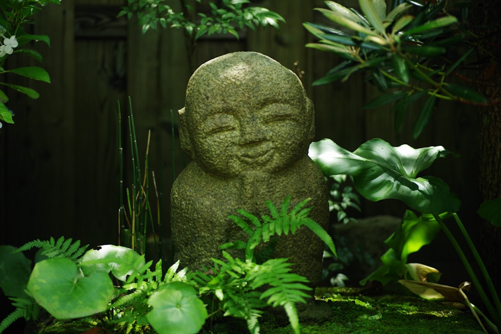 Una estatua de piedra de Buda en un jardín rodeado de plantas