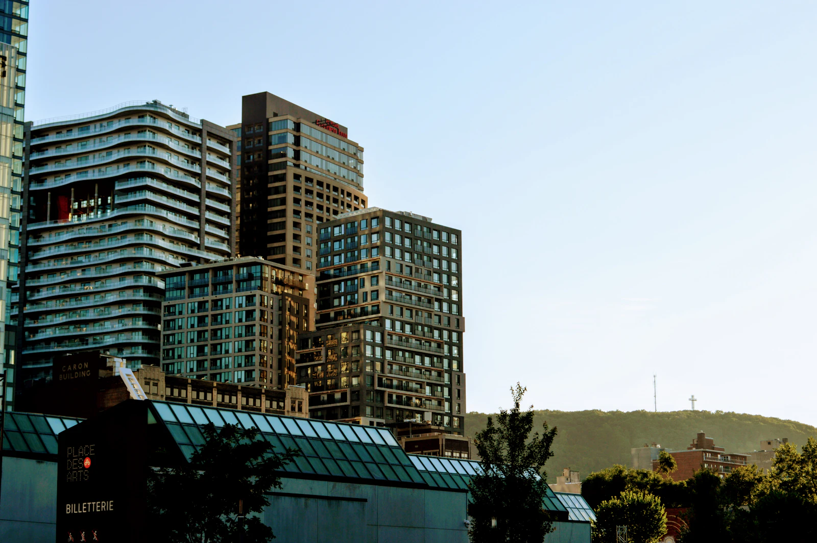 The downtown Montreal skyline at dusk with the Place des Arts complex in the foreground and the lit cross atop Mount Royal in the distance