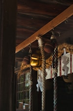 A traditional Japanese Shinto shrine featuring thick ropes, a large golden bell, and paper decorations known as shide. The structure is made of dark wood with intricate patterns, creating a serene and sacred atmosphere.