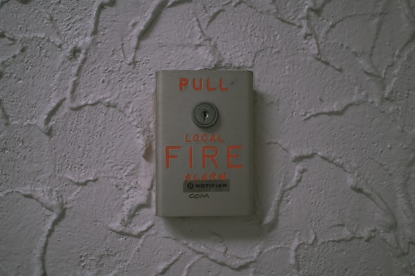A fire alarm pull station is mounted on a textured wall. The device is metallic with bright red text indicating 'PULL' and 'LOCAL FIRE ALARM,' displaying a clear instruction for emergency use.