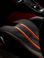 A detailed view of a car's interior, showcasing a high-end seat with a black and red color scheme. The seat features sleek black leather with vibrant red accents and stitching, highlighting a luxurious and sporty design. Part of the console is visible, emphasizing modern and sophisticated aesthetics.