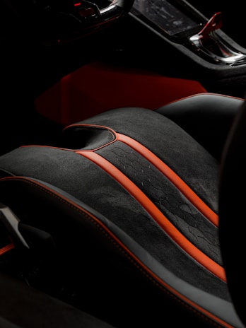 A detailed view of a car's interior, showcasing a high-end seat with a black and red color scheme. The seat features sleek black leather with vibrant red accents and stitching, highlighting a luxurious and sporty design. Part of the console is visible, emphasizing modern and sophisticated aesthetics.
