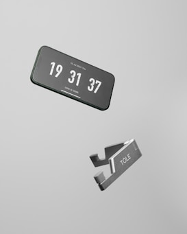 A smartphone displaying the current time floating in mid-air, next to a metallic object labeled 'TOLE'. The background is a plain light gray, emphasizing the minimalist design.