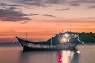 A rustic wooden boat anchored near a quiet island cove at golden hour.