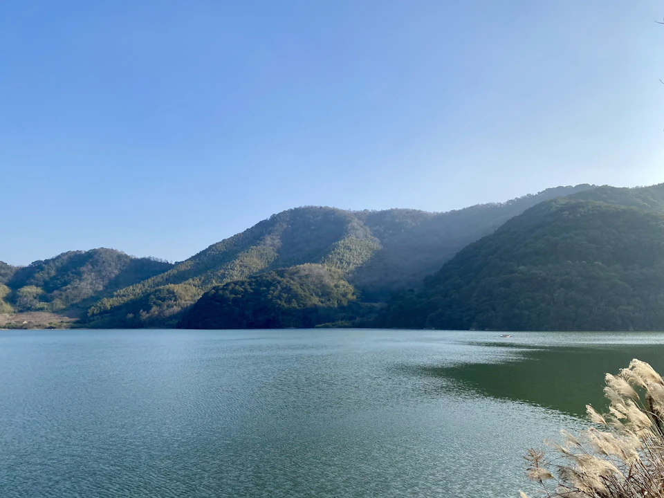Serene lake nestled in lush green mountains with calm light blue water reflecting clear sky