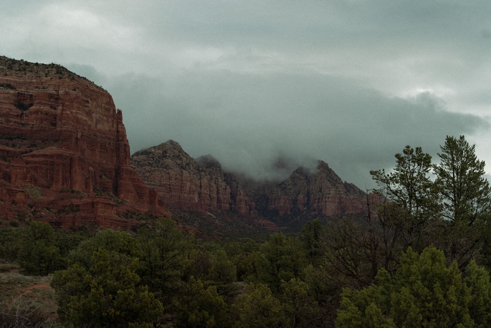 a mountain range with trees in the foreground and clouds in the background