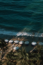 an aerial view of a beach with umbrellas and palm trees