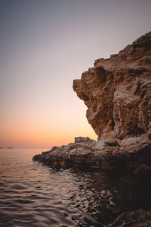 Rugged cliffs overlooking the deep blue Mediterranean Sea with a warm sunset casting orange hues