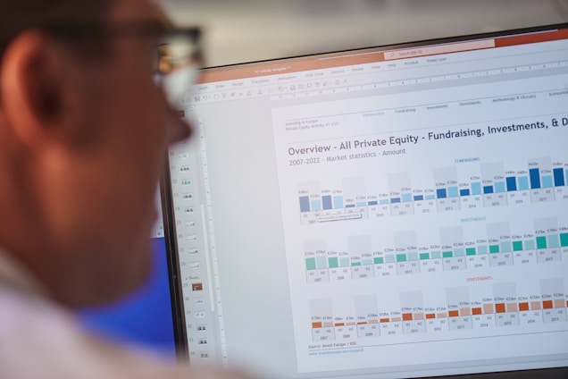 A person is looking at a computer screen displaying a document titled 'Overview - All Private Equity - Fundraising, Investments, & D'. The document contains statistical charts and graphs related to private equity market statistics from 2007 to 2022. Various tabs and functions like 'File', 'Home', 'Insert', and 'Design' are visible in the interface.