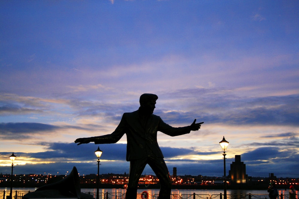 a statue of a man holding his arms out in front of a body of water