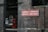 A vintage railway station scene with a prominent brick wall displaying a directional sign for London and Holyhead. A classic red British telephone box is visible next to an arched window and a station bench.