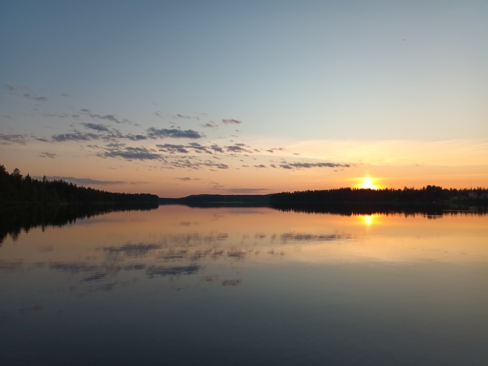 the sun is setting over a calm lake