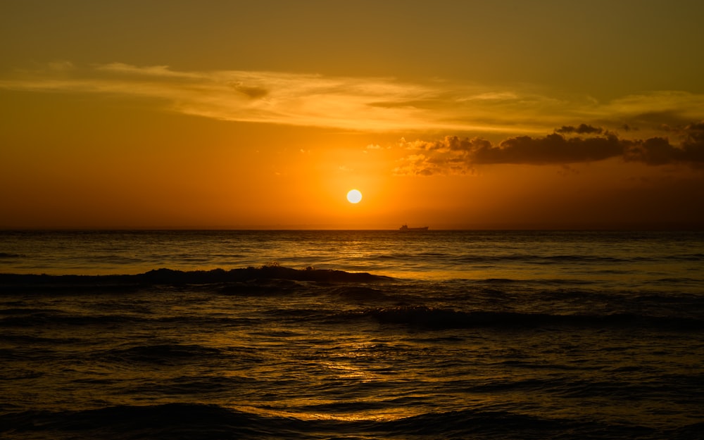 a sunset over the ocean with a boat in the distance