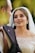 A bride wearing an elegant, beaded white wedding dress gazes lovingly at someone in a black suit. Her makeup is elaborate, and she wears a pearl-covered veil.