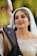 A bride wearing an elegant, beaded white wedding dress gazes lovingly at someone in a black suit. Her makeup is elaborate, and she wears a pearl-covered veil.