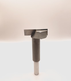 A metal tool with a cylindrical handle and a sharp, angular cutting head is positioned vertically against a plain, light background. The tool appears to be designed for precision cutting or boring tasks.