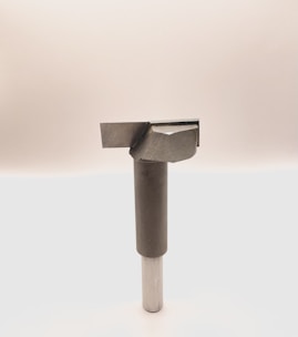 A metal tool with a cylindrical handle and a sharp, angular cutting head is positioned vertically against a plain, light background. The tool appears to be designed for precision cutting or boring tasks.