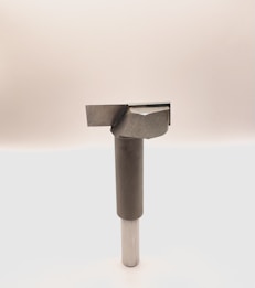 A metal tool with a cylindrical handle and a sharp, angular cutting head is positioned vertically against a plain, light background. The tool appears to be designed for precision cutting or boring tasks.