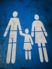 White silhouettes of two adults and a child holding hands are painted on a blue textured surface, typically indicating a family parking space.