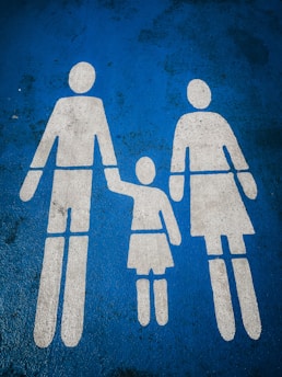 White silhouettes of two adults and a child holding hands are painted on a blue textured surface, typically indicating a family parking space.