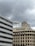 Several buildings with industrial and commercial designs stand under an overcast sky. An architectural structure features numerous antennas and communication devices on its rooftop.