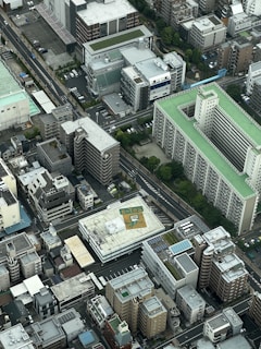 The aerial view captures a densely packed urban area with various multi-story buildings. The architecture includes both residential and commercial structures with flat rooftops. Some rooftops have solar panels, and one prominently features an 'e-tax' logo. The scene is dominated by concrete and asphalt but is interspersed with patches of greenery.