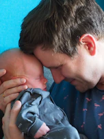 A quiet moment of a father softly kissing his newborn’s forehead, surrounded by calm beige tones.
