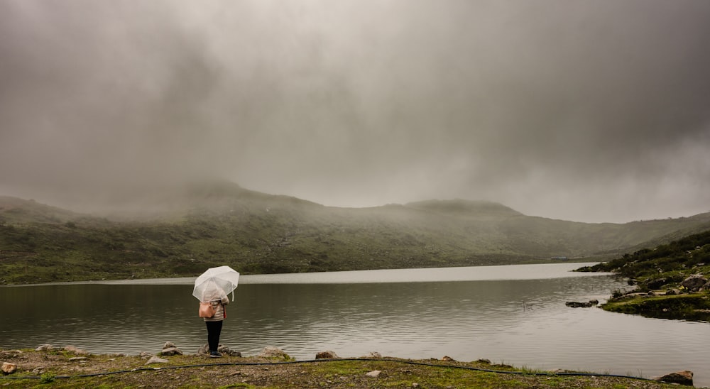 a person with an umbrella standing by a lake