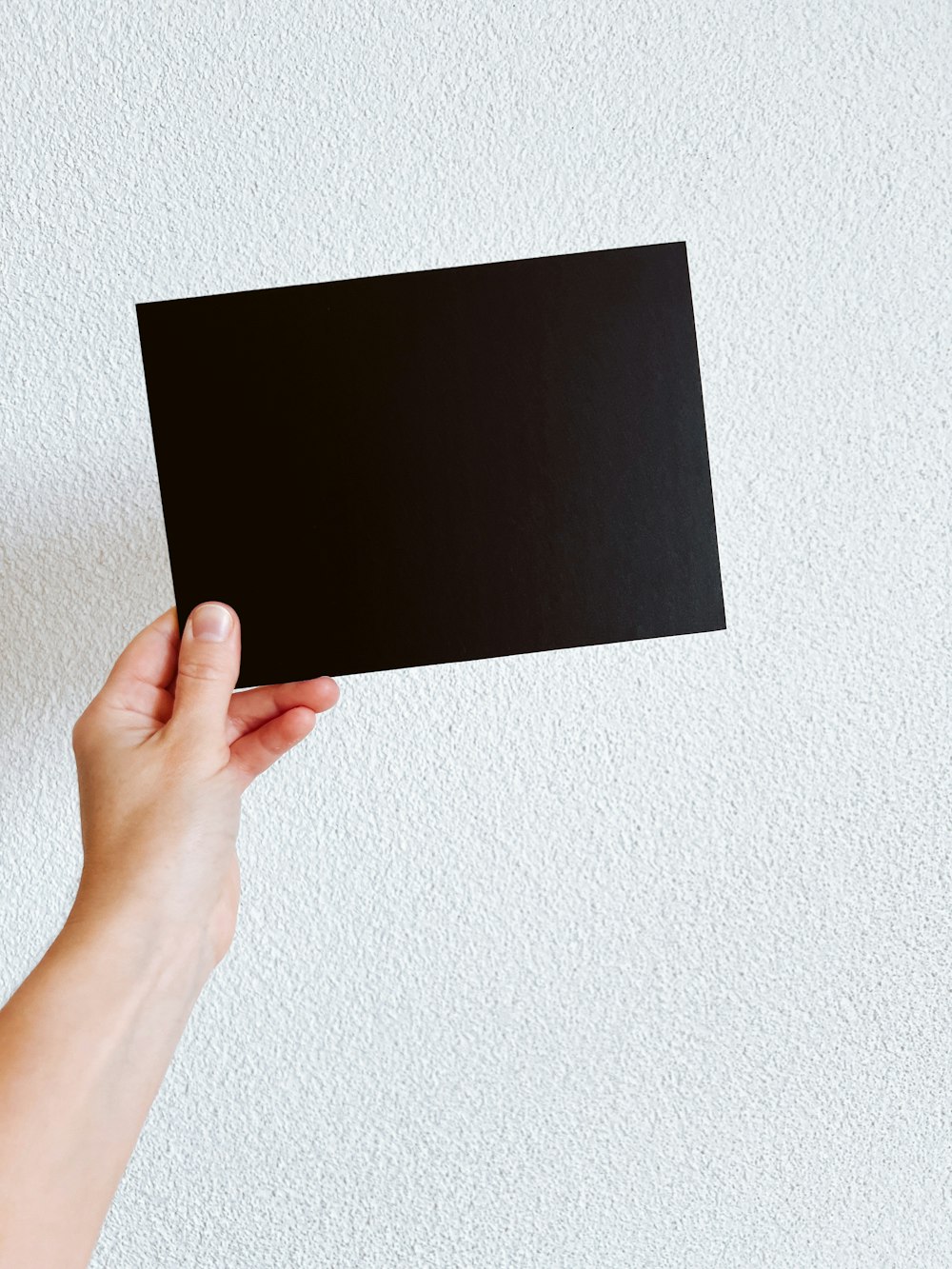 a person holding up a black square piece of paper