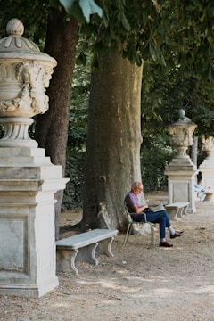 A man reading a book under a large oak tree in a quiet park.