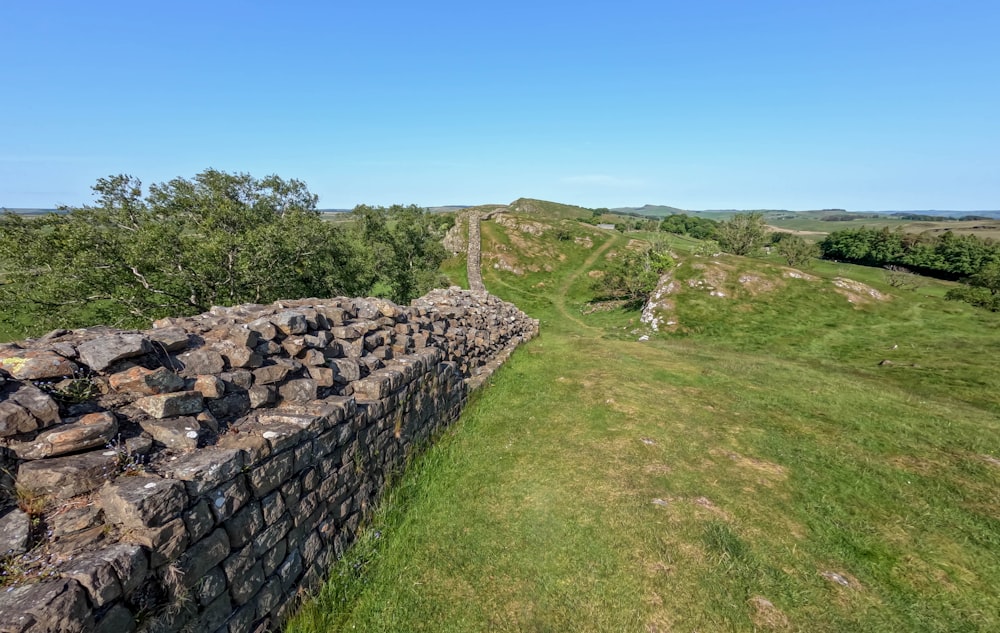 a stone wall in the middle of a grassy field