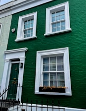 a green building with white windows and a black fence