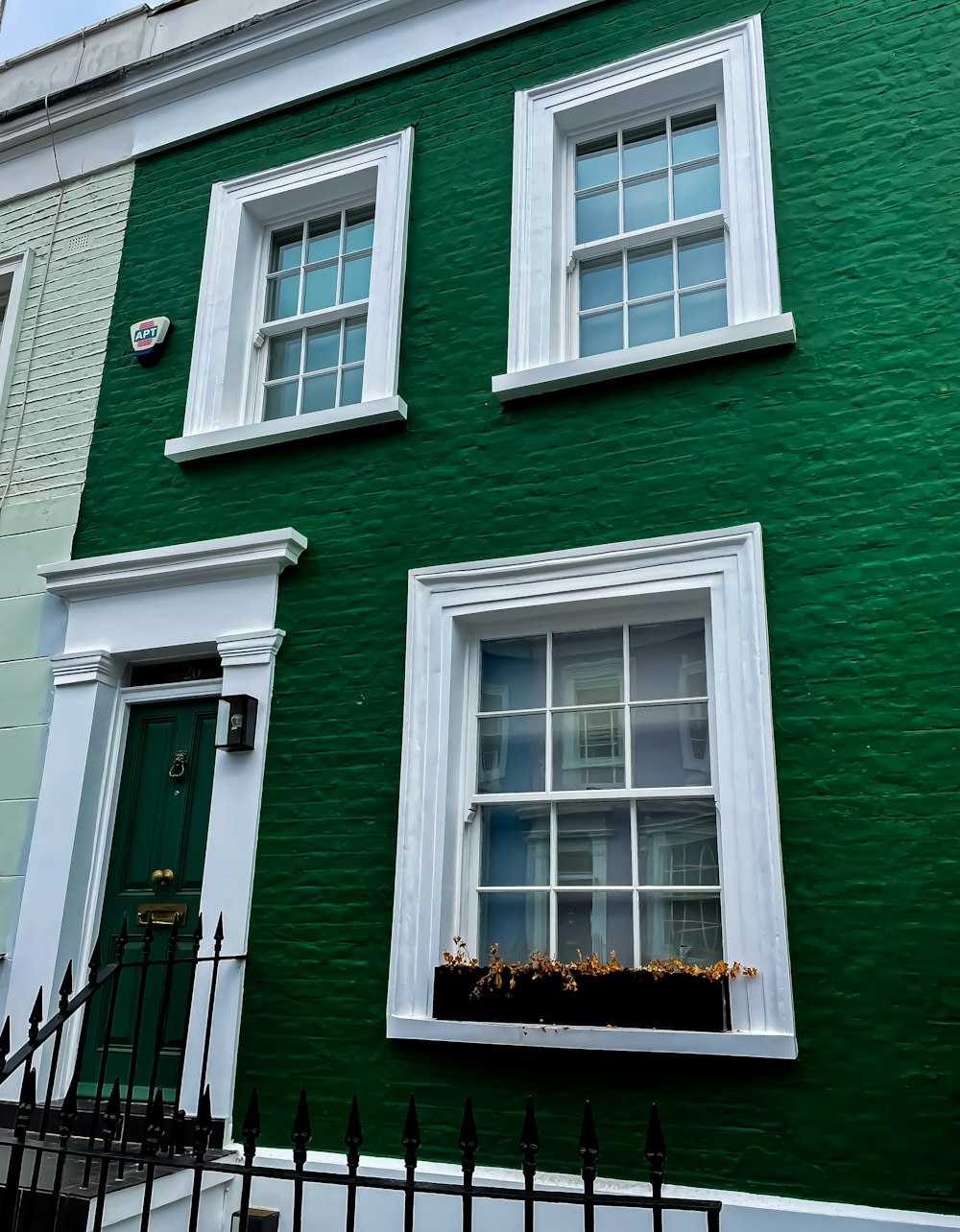 a green building with white windows and a black fence