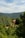 A rustic stone house with a red-tiled roof is nestled among lush green forests and rolling hills under a partly cloudy sky. The landscape is serene and abundant with verdant trees, creating a peaceful and secluded atmosphere.