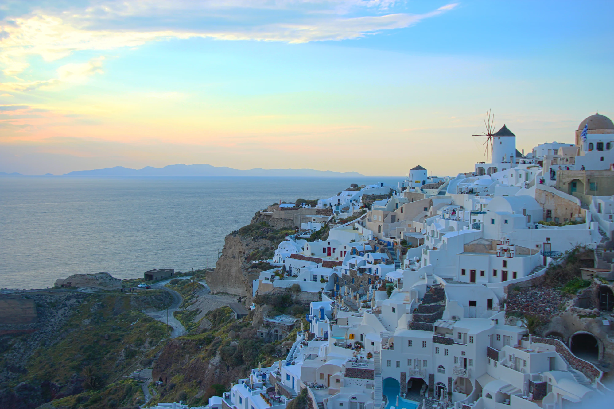 Whitewashed village on the rim of the Santorini caldera at golden hour, with a windmill above the sea