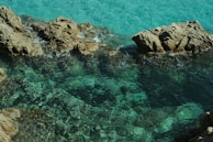 Crystal-clear turquoise waters gently lapping against smooth rocks on a sunny day.