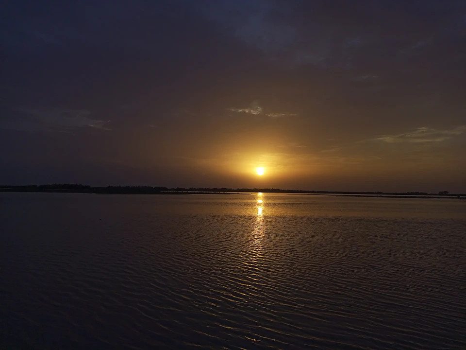 Serene sunset over calm waters reflects vibrant sunset hues behind the horizon line
