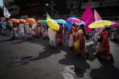 Colorful festival procession with dancers in traditional attire carrying ornate umbrellas.
