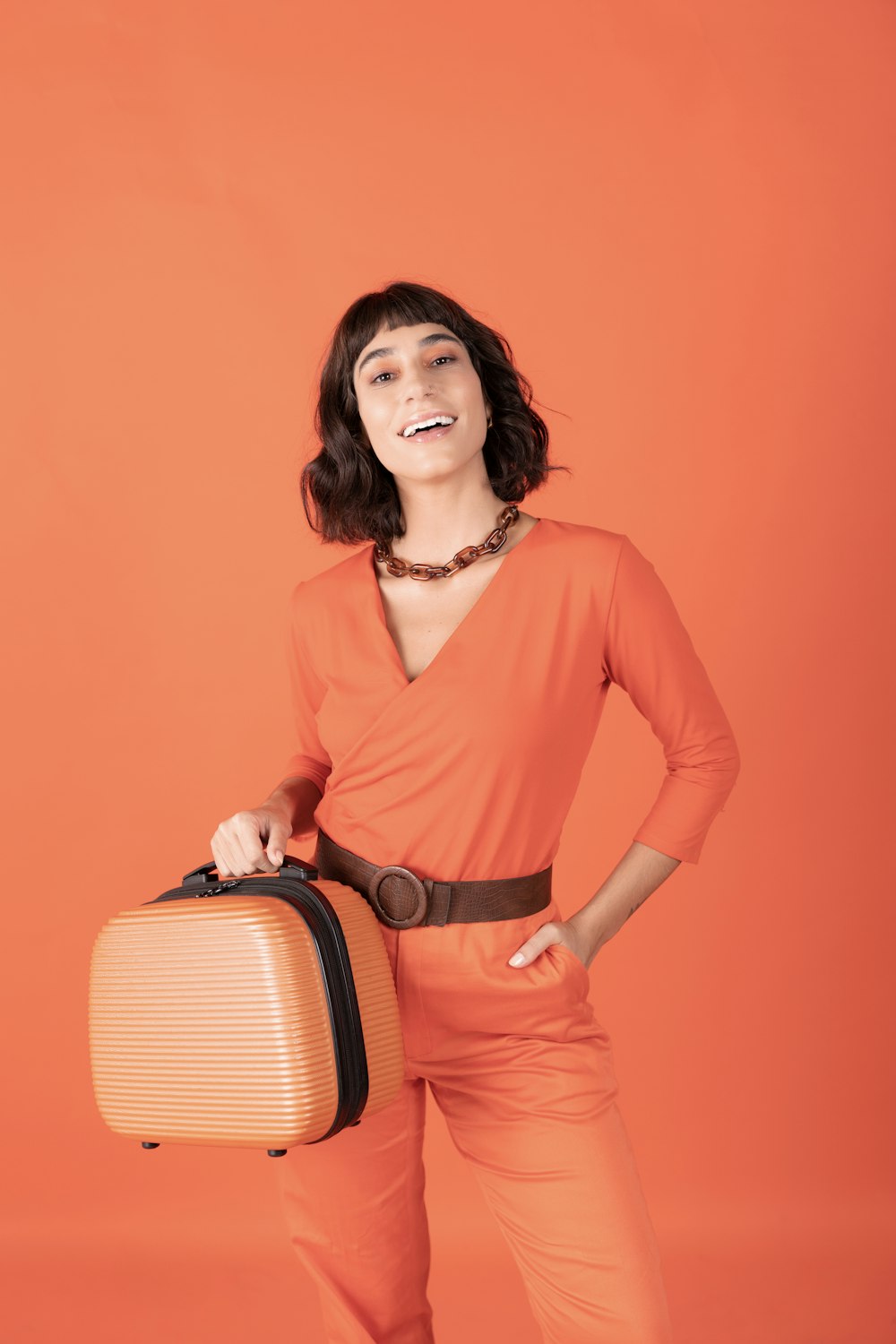 a woman in an orange jumpsuit holding a suitcase