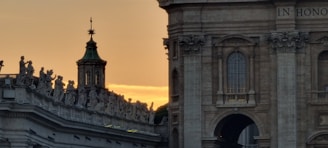 A detailed architectural scene featuring an ornate building with intricate sculptures adorning the roofline. The background is lit by a warm golden sunset, casting a serene glow on the stone surfaces.