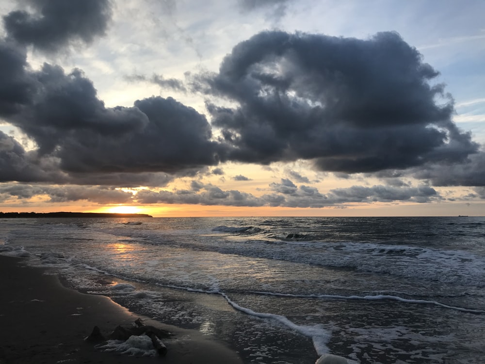 the sun is setting over the ocean on a cloudy day