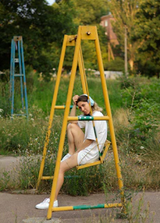 a woman sitting on a yellow swing in a park
