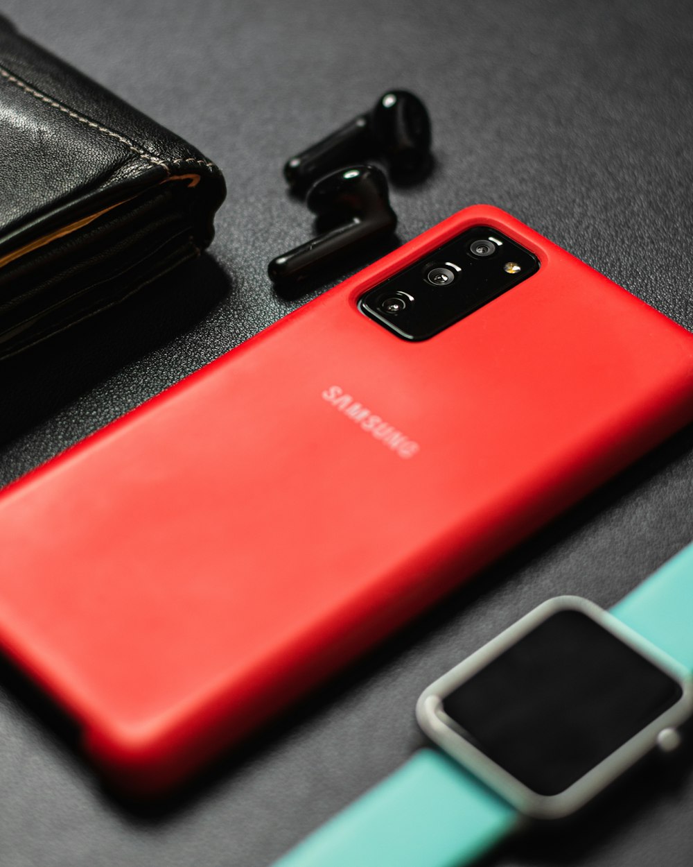 Um telefone Samsung vermelho sentado em cima de uma mesa ao lado de uma carteira