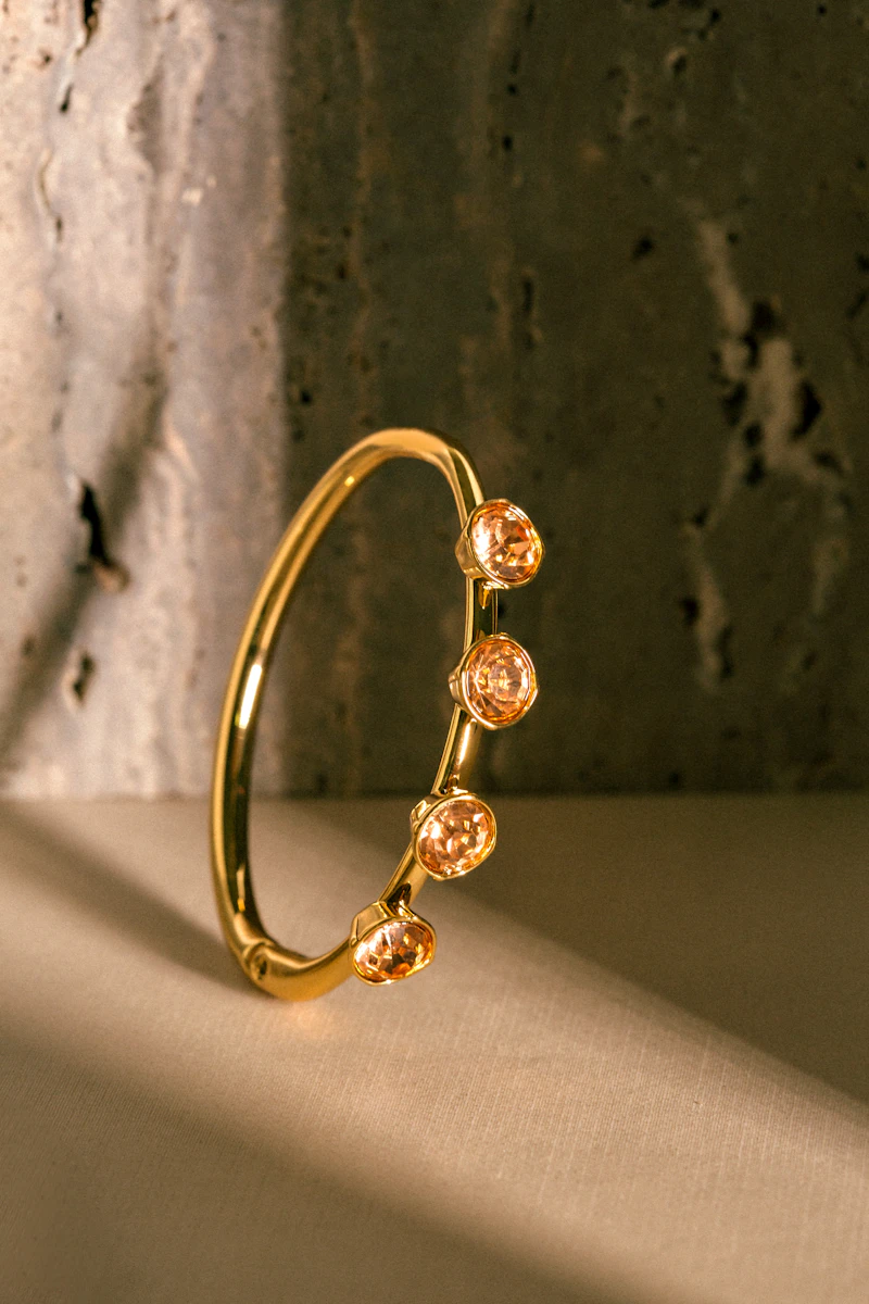 Polished gold open bangle with round stone accents on a warm stone surface