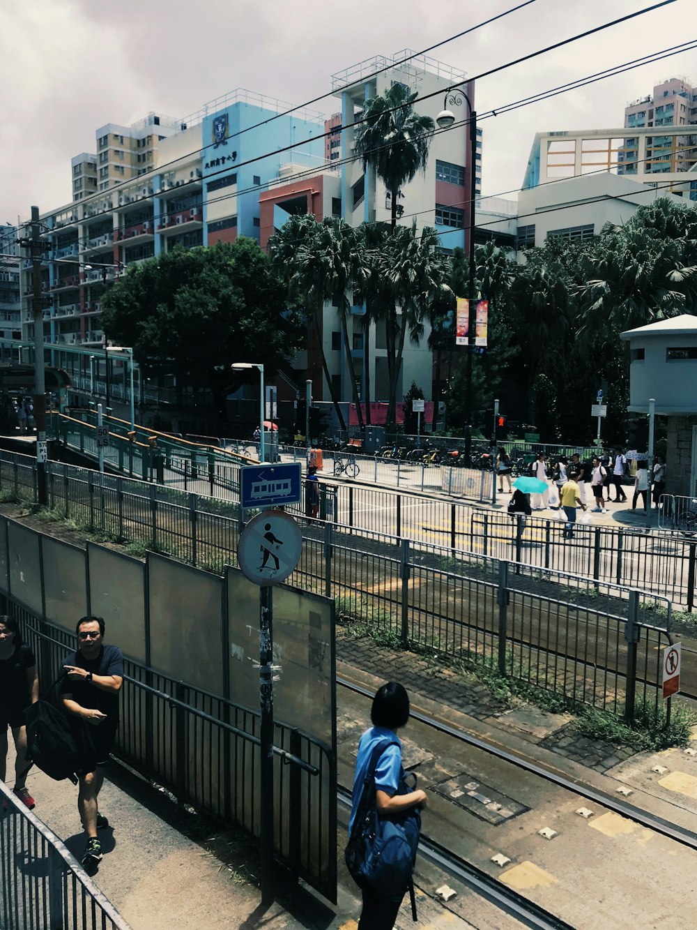 a group of people walking down a street next to a fence