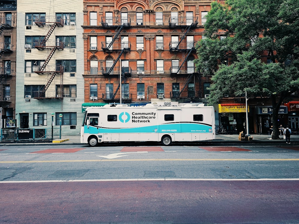 a white and blue bus parked in front of a tall building