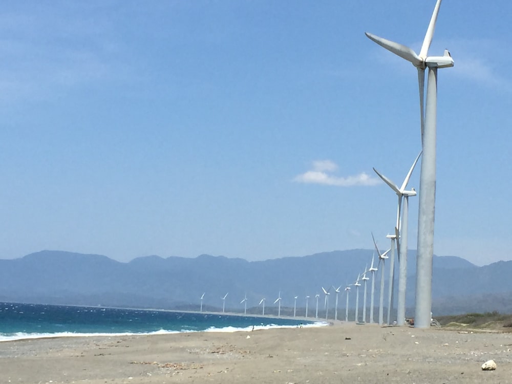 a row of wind turbines next to the ocean