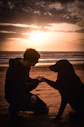 a man kneeling down next to a dog on a beach